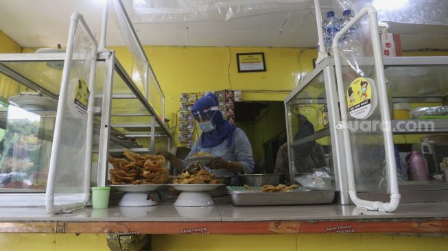 Pemilik warteg melayani pembeli di warteg yang menerapkan protokol kesehatan di kawasan Cilandak Timur, Jakarta Selatan, Senin (20/7/2020). [Suara.com/Angga Budhiyanto]