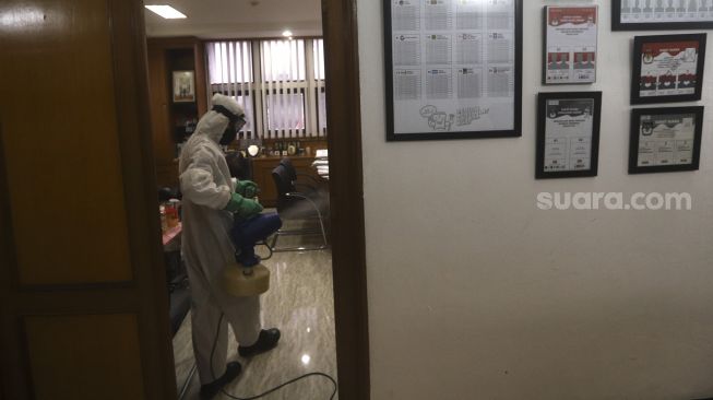 Petugas menyemprotkan cairan disinfektan di gedung Komisi Pemilihan Umum (KPU) Republik Indonesia, Jakarta, Selasa (21/7/2020). [Suara.com/Angga Budhiyanto]