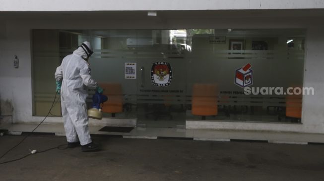 Petugas menyemprotkan cairan disinfektan di gedung Komisi Pemilihan Umum (KPU) Republik Indonesia, Jakarta, Selasa (21/7/2020). [Suara.com/Angga Budhiyanto]