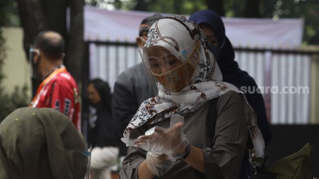 Seorang pemilih mengenakan sarung tangan sebelum melakukan pencoblosan surat suara di bilik suara saat simulasi pemungutan suara Pilkada Serentak 2020 di Kantor Komisi Pemilihan Umum (KPU) Republik Indonesia, Jakarta, Rabu (22/72020). [Suara.com/Angga Budhiyanto]