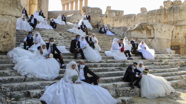 Sejumlah pasangan pengantin mengenakan masker wajah duduk di tangga selama acara pernikahan bersama di tengah pandemi Covid-19 di Kuil Bacchus di situs bersejarah Baalbek di Lembah Bekaa, Lebanon Timur, Jumat (24/7/2020). [AFP]