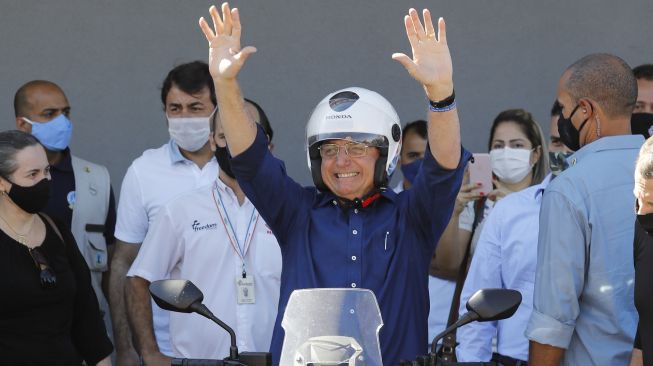 Presiden Brasil Jair Bolsonaro memberi isyarat setelah pergi menaiki sepeda motornya di Brasilia, Sabtu (25/7/2020). [Sergio Lima / AFP]