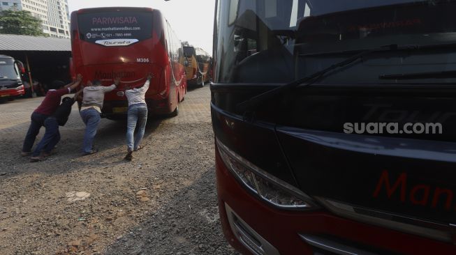 Sejumlah mekanik mendorong bus di salah satu pool bus pariwisata di kawasan Tanjung Barat, Jagakarsa, Jakarta, Selasa (28/7/2020). [Suara.com/Angga Budhiyanto]