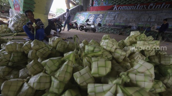 Pedagang menyelesaikan pembuatan kulit ketupat bawah jalan tol di kawasan Bintaro, Jakarta, Kamis (30/7/2020). [Suara.com/Angga Budhiyanto]