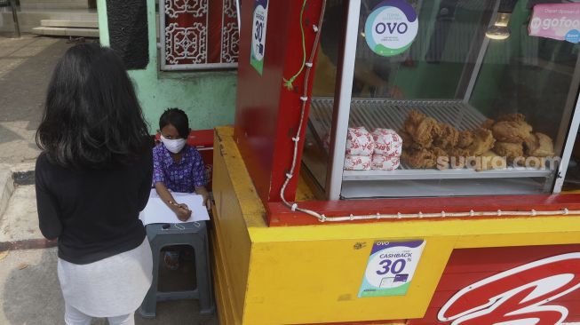 Siswi kelas 2 SDN 01 Pagi Bukit Duri Keysha Nayara Effeni (8) belajar secara online di gerai makanan tempat Ibunya berjualan di kawasan Bukit Duri, Jakarta, Kamis (30/7/2020). [Suara.com/Angga Budhiyanto]