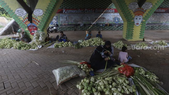 Pedagang menyelesaikan pembuatan kulit ketupat di bawah jalan tol di kawasan Bintaro, Jakarta, Kamis (30/7/2020). [Suara.com/Angga Budhiyanto]