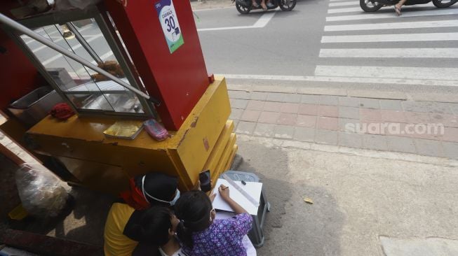 Siswi kelas 2 SDN 01 Pagi Bukit Duri Keysha Nayara Effeni (8) belajar secara online ditemani ibunya Okta (31) di gerai makanan tempat Ibunya berjualan di kawasan Bukit Duri, Jakarta, Kamis (30/7/2020). [Suara.com/Angga Budhiyanto]