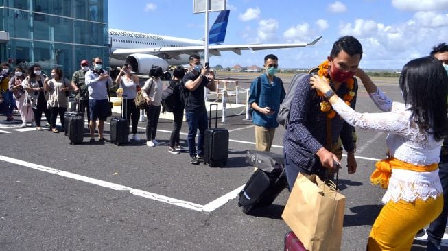 Petugas mengalungkan bunga untuk menyambut penumpang pesawat rute domestik yang tiba di Bandara Internasional I Gusti Ngurah Rai, Badung, Bali, Jumat (31/7/2020).  [ANTARA FOTO/Fikri Yusuf]