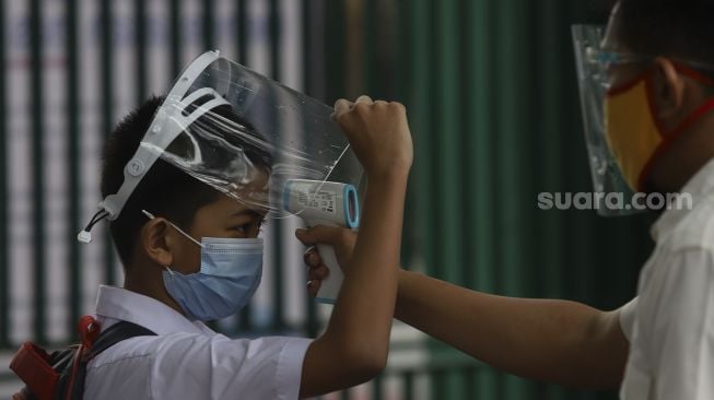 Guru memeriksa suhu tubuh siswa sebelum memasuki ruang kelas di SDN Pekayon Jaya VI, Kota Bekasi, Jawa Barat, Selasa (4/8/2020). [Suara.com/Angga Budhiyanto]