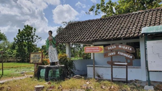 Patung penjual jamu gendong dan petunjuk arah yang terpasang di jalan sebelum masuk ke Desa Wisata Jamu Gendong Kiringan, Desa Canden, Jetis, Bantul, Selasa (4/8/2020). [Suara.com/Hiskia]