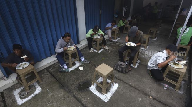 Sejumlah warga menyantap hidangan makan gratis di Jalan Jenderal Basuki Rachmat, Cipinang Besar Selatan, Jakarta, Rabu (5/8/2020). [Suara.com/Angga Budhiyanto]