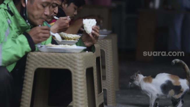 Sejumlah warga menyantap hidangan makan gratis di Jalan Jenderal Basuki Rachmat, Cipinang Besar Selatan, Jakarta, Rabu (5/8/2020). [Suara.com/Angga Budhiyanto]