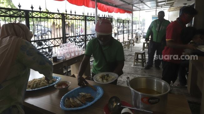 Petugas melayani warga yang hendak menyantap hidangan makan gratis di Jalan Jenderal Basuki Rachmat, Cipinang Besar Selatan, Jakarta, Rabu (5/8/2020). [Suara.com/Angga Budhiyanto]