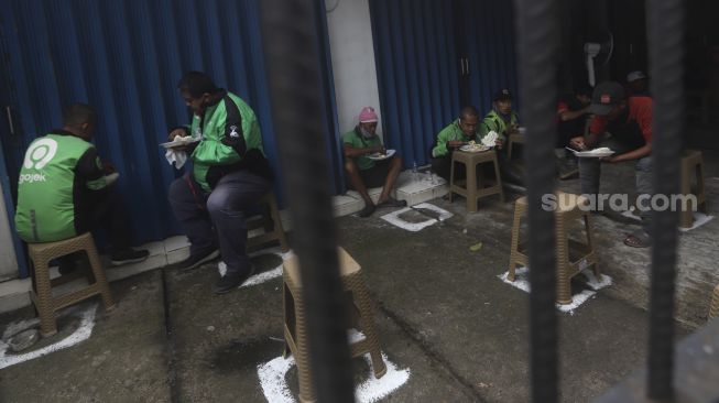 Sejumlah warga menyantap hidangan makan gratis di Jalan Jenderal Basuki Rachmat, Cipinang Besar Selatan, Jakarta, Rabu (5/8/2020). [Suara.com/Angga Budhiyanto]