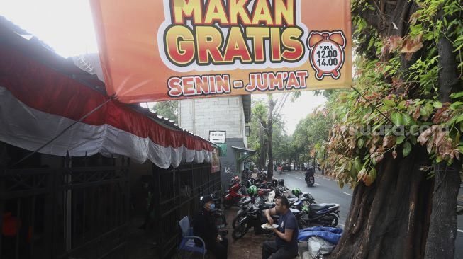 Seorang warga menyantap hidangan makan gratis di Jalan Jenderal Basuki Rachmat, Cipinang Besar Selatan, Jakarta, Rabu (5/8/2020). [Suara.com/Angga Budhiyanto]