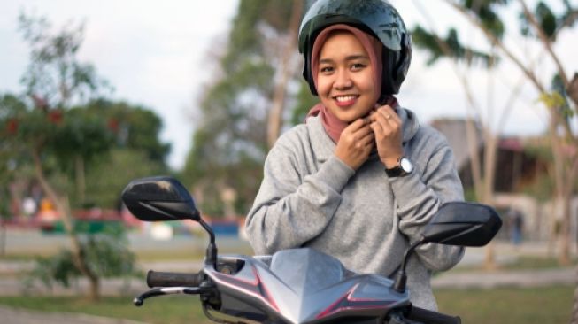 Hijaber mengenakan helm, siap mengaspal dengan motor matik. Sebagai ilustrasi [Shutterstock].