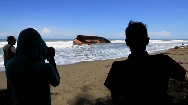 Warga melihat kapal tongkang pengangkut batu bara yang terdampar di Kawasan Pantai Naga Permai Desa Gampong Lhok, Kecamatan Kuala Pesisir, Nagan Raya, Aceh, Jumat (7/8/2020).  [ANTARA FOTO/Syifa Yulinnas]