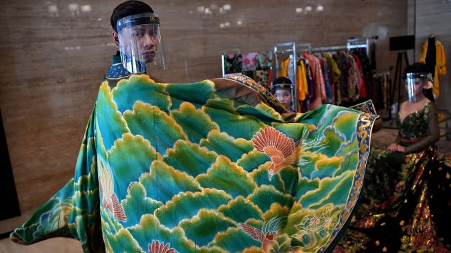 Model pria mengenakan pelindung wajah melakukan peragaan busana pengantin tradisional bermotif batik di Surabaya, Jawa Timur, Kamis (6/8/2020).  [FOTO/Zabur Karuru]