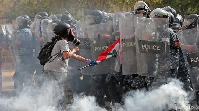 Demonstran Lebanon mengibarkan bendera nasional selama bentrokan di Beirut, Sabtu (8/8/2020) (AFP/ Anwar Amro)