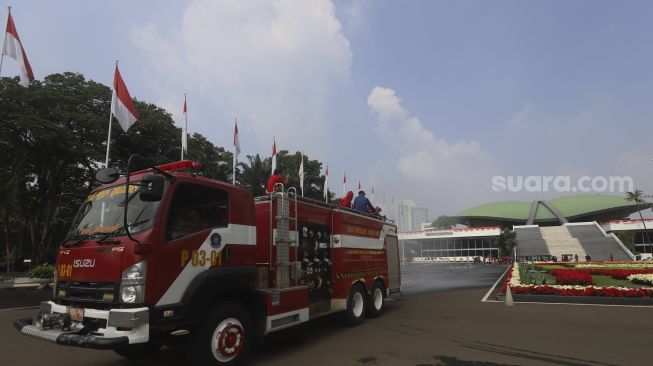 Petugas pemadam kebakaran menyemprotkan cairan disinfektan di area komplek Gedung DPR/MPR RI, Jakarta, Minggu (9/8/2020). [Suara.com/Angga Budhiyanto]