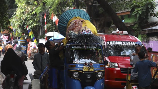 Warga menaikkan ondel-ondel ke atas bajaj di Kampung Ondel-ondel, Jalan Kembang Pacar, Senen, Jakarta, Rabu (12/8/2020). [Suara.com/Angga Budhiyanto]