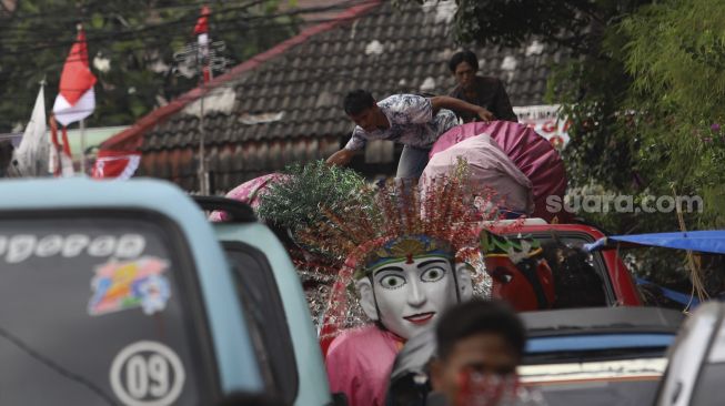 Warga menaikkan ondel-ondel ke atas mobil angkutan umum di Kampung Ondel-ondel, Jalan Kembang Pacar, Senen, Jakarta, Rabu (12/8/2020). [Suara.com/Angga Budhiyanto]