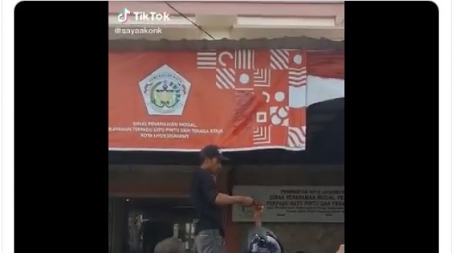 Seorang pria mengecat spanduk peringatan HUT RI ke 75 di Kantor Dinas Penanaman Modal Lhokseumawe. - (Twitter/@tubirfess)