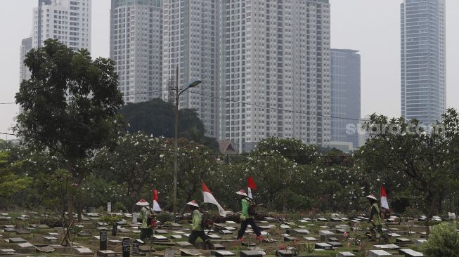 Petugas Pertamanan dan Kehutanan Kota Jakarta Pusat berjalan mengenakan atribut kemerdekaan usai memangkas rumput di TPU Karet Bivak, Tanah Abang, Jakarta Pusat, Minggu (16/8/2020). [Suara.com/Angga Budhiyanto]