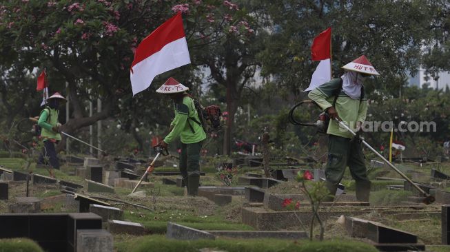 Petugas Pertamanan dan Kehutanan Kota Jakarta Pusat mengenakan atribut kemerdekaan saat memangkas rumput di TPU Karet Bivak, Tanah Abang, Jakarta Pusat, Minggu (16/8/2020). [Suara.com/Angga Budhiyanto]