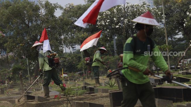 Petugas Pertamanan dan Kehutanan Kota Jakarta Pusat mengenakan atribut kemerdekaan saat memangkas rumput di TPU Karet Bivak, Tanah Abang, Jakarta Pusat, Minggu (16/8/2020). [Suara.com/Angga Budhiyanto]