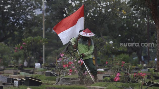 Seorang petugas Pertamanan dan Kehutanan Kota Jakarta Pusat mengenakan atribut kemerdekaan saat memangkas rumput di TPU Karet Bivak, Tanah Abang, Jakarta Pusat, Minggu (16/8/2020). [Suara.com/Angga Budhiyanto]