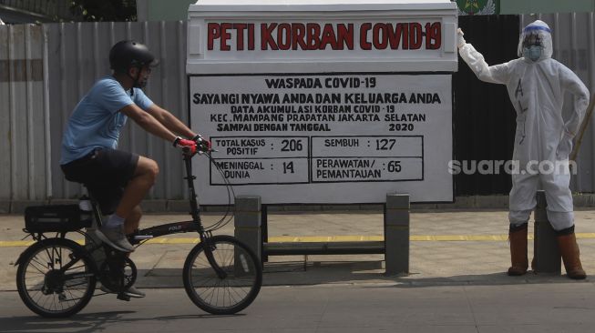 Pesepeda melintas di depan seni instalasi tenaga medis yang sedang memegang peti jenazah korban COVID-19 di simpang jalan Kemang 1, Jakarta Selatan, Minggu (16/8/2020). [Suara.com/Angga Budhiyanto]