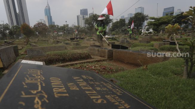 Petugas Pertamanan dan Kehutanan Kota Jakarta Pusat mengenakan atribut kemerdekaan saat memangkas rumput di TPU Karet Bivak, Tanah Abang, Jakarta Pusat, Minggu (16/8/2020). [Suara.com/Angga Budhiyanto]