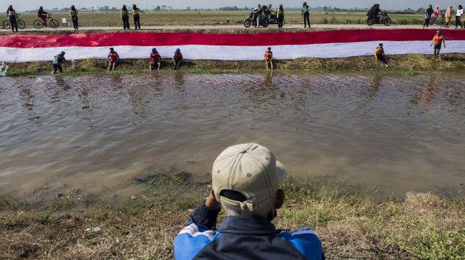 Komunitas Pasukan Susur Sungai dan Ekosistem Rancaekek (Passer) membentangkan kain Merah Putih di bantaran sungai Cikijing, Rancaekek, Kabupaten Bandung, Jawa Barat, Minggu (16/8/2020). [ANTARA FOTO/M Agung Rajasa]