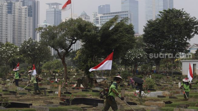 Petugas Pertamanan dan Kehutanan Kota Jakarta Pusat mengenakan atribut kemerdekaan saat memangkas rumput di TPU Karet Bivak, Tanah Abang, Jakarta Pusat, Minggu (16/8/2020). [Suara.com/Angga Budhiyanto]