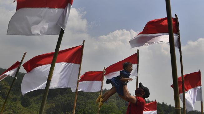 Pengunjung bermain bersama anaknya di antara bendera Merah Putih yang dipasang di Poetoek Suko, Trawas, Mojokerto, Jawa Timur, Minggu (16/8/2020). [ANTARA FOTO/Zabur Karuru]