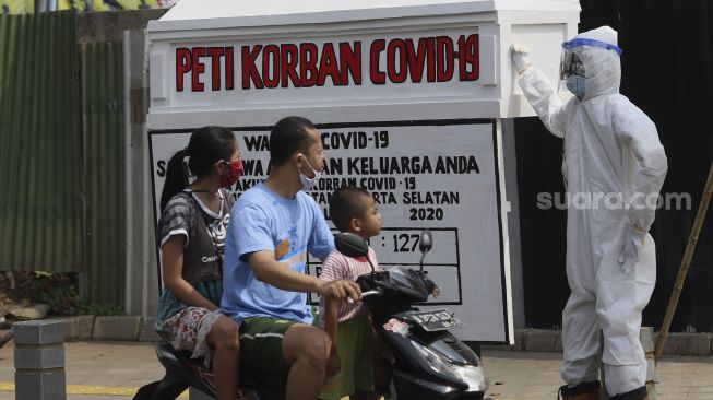 Pengendara sepeda motor melintas di depan seni instalasi tenaga medis yang sedang memegang peti jenazah korban COVID-19 di simpang jalan Kemang 1, Jakarta Selatan, Minggu (16/8/2020). [Suara.com/Angga Budhiyanto]