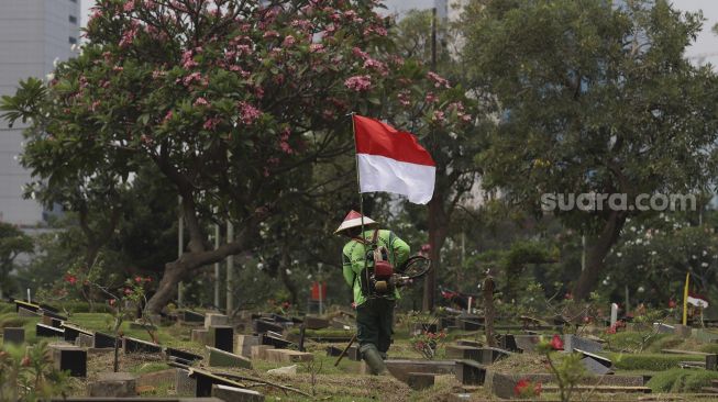 Seorang petugas Pertamanan dan Kehutanan Kota Jakarta Pusat mengenakan atribut kemerdekaan saat memangkas rumput di TPU Karet Bivak, Tanah Abang, Jakarta Pusat, Minggu (16/8/2020). [Suara.com/Angga Budhiyanto]