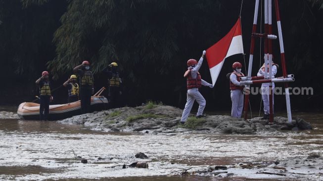 Petugas upacara mengibarkan bendera Merah Putih saat melaksanakan upacara bendera di Sungai Ciliwung, GDC, Depok, Jawa Barat, Senin (17/8/2020). [Suara.com/Angga Budhiyanto]