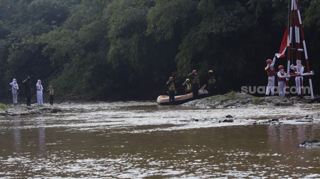 Petugas upacara mengibarkan bendera Merah Putih saat melaksanakan upacara bendera di Sungai Ciliwung, GDC, Depok, Jawa Barat, Senin (17/8/2020). [Suara.com/Angga Budhiyanto]