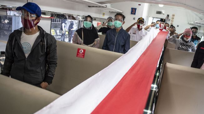 Penumpang mengikuti proses pembentangan bendera Merah Putih di dalam rangkaian KA Serayu di Peron 1 Stasiun Pasar Senen, Jakarta, Senin (17/8/2020). [ANTARA FOTO/Aprillio Akbar]