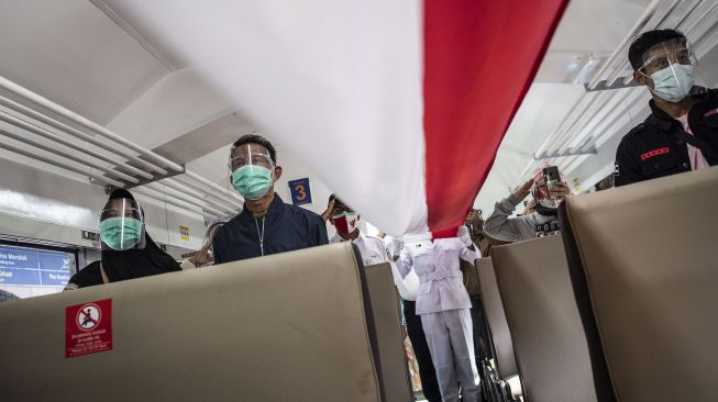 Penumpang mengikuti proses pembentangan bendera Merah Putih di dalam rangkaian KA Serayu di Peron 1 Stasiun Pasar Senen, Jakarta, Senin (17/8/2020). [ANTARA FOTO/Aprillio Akbar]