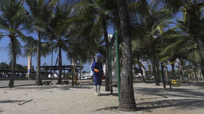 Seorang petugas menyemprotkan cairan disinfektan di kawasan pantai Ancol, Jakarta Utara, Jumat (21/8/2020). [Suara.com/Angga Budhiyanto]