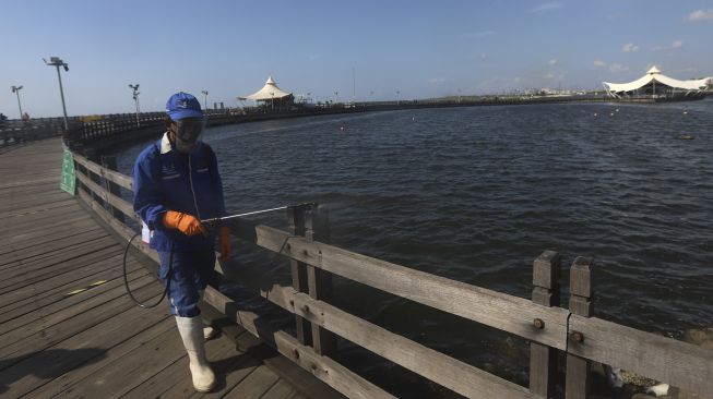 Seorang petugas menyemprotkan cairan disinfektan di kawasan pantai Ancol, Jakarta Utara, Jumat (21/8/2020). [Suara.com/Angga Budhiyanto]