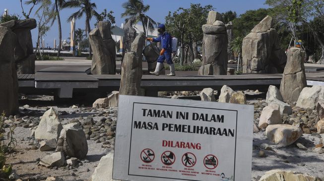 Seorang petugas menyemprotkan cairan disinfektan di kawasan pantai Ancol, Jakarta Utara, Jumat (21/8/2020). [Suara.com/Angga Budhiyanto]