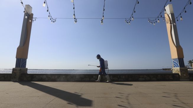 Seorang petugas menyemprotkan cairan disinfektan di kawasan pantai Ancol, Jakarta Utara, Jumat (21/8/2020). [Suara.com/Angga Budhiyanto]