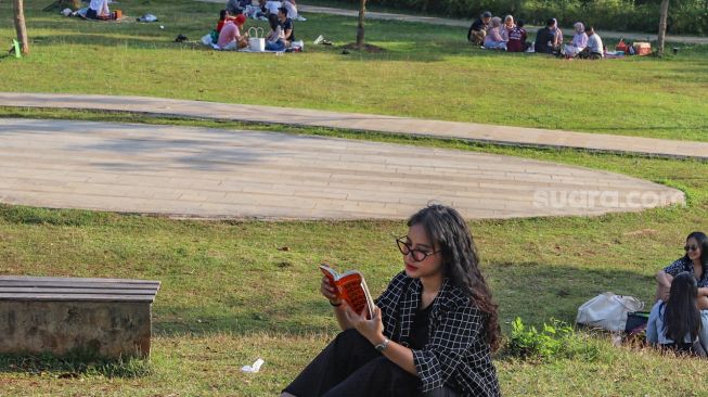 Seorang warga menghabiskan waktinya dengan membaca buku di area Hutan Kota Gelora Bung Karno, Senayan, Jakarta Sekatan, Minggu (23/8). [Suara.com/Alfian Winanto]