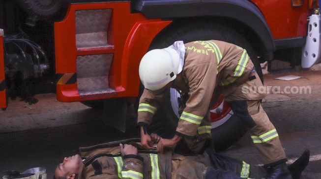 Petugas Damkar DKI kelelahan usai melakukan proses pendinginan di Gedung Utama Kejaksaan Agung RI di Jalan Sultan Hasanuddin, Jakarta Selatan, Minggu (23/8). [Suara.com/Alfian Winanto]