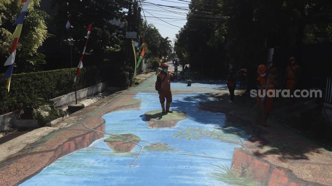 Petugas PPSU membersihkan area jalan yang dihiasi mural 3D di sepanjang Jalan Keuangan Raya, Cilandak Barat, Jakarta Selatan, Selasa (25/8/2020). [Suara.com/Angga Budhiyanto]