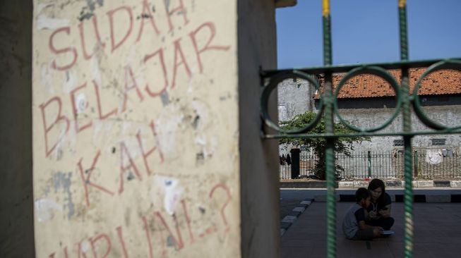 Orang tua siswa membimbing anaknya belajar daring memanfaatkan jaringan internet gratis di kolong rel kereta api Mangga Besar, Jakarta, Rabu (26/8/2020).  [ANTARA FOTO/Nova Wahyudi]